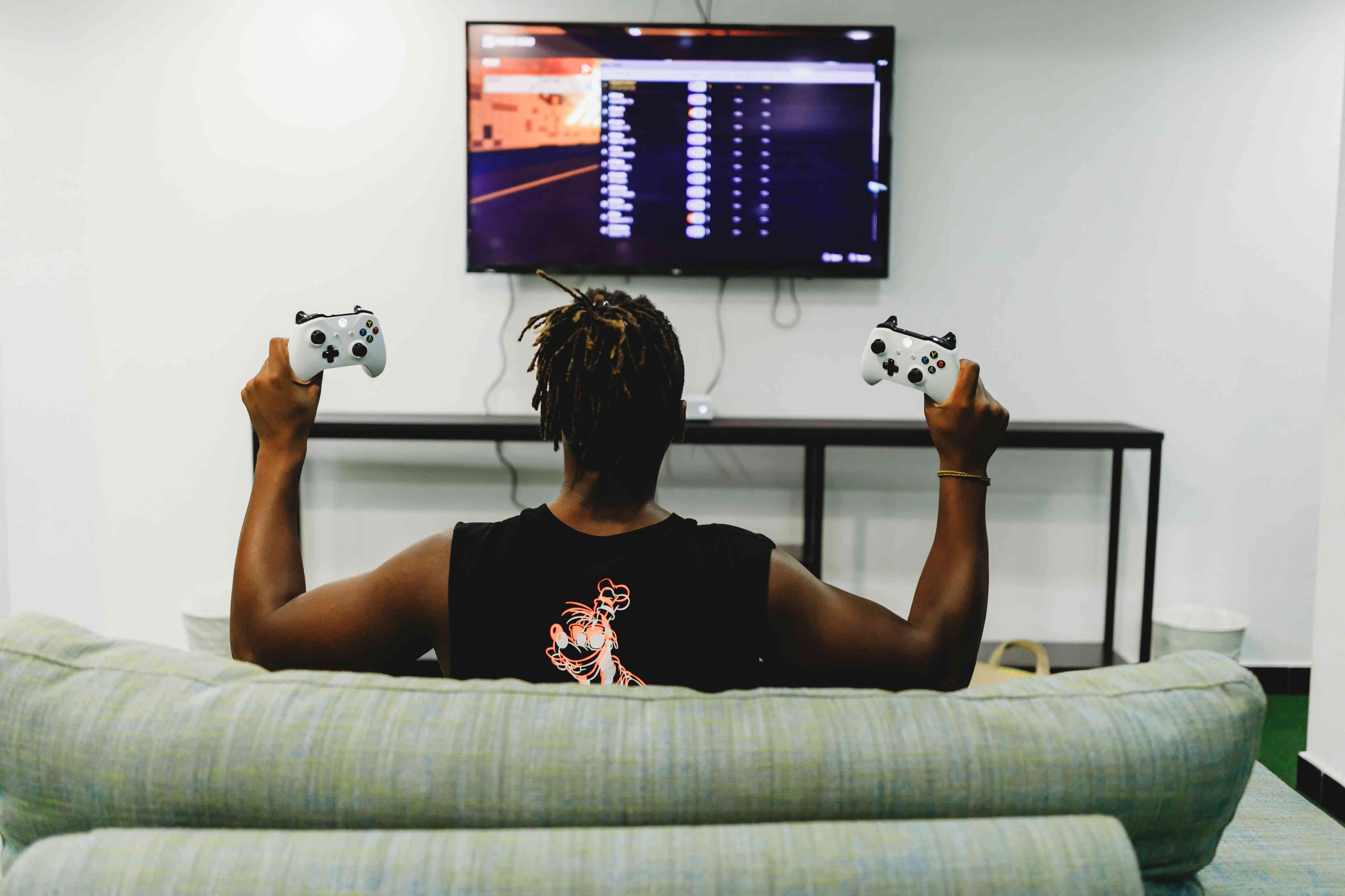 Una vista desde atrás de alguien jugando Xbox, sosteniendo un controlador en cada mano.
